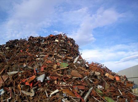 Large mound of scrap metal and wood piled outdoors against a blue sky.
