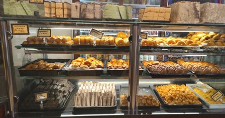 Glass bakery display case filled with trays of croissants, pastries and donuts on three shelves, ready for sale.