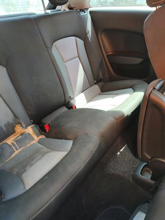 Rear car seat with black/gray fabric shows a large tear on the left side, exposing padding; dirty floor and scuffed upholstery visible in the back of the vehicle.