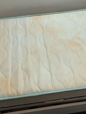 Close-up of a white quilted mattress with a light blue edging, photographed from the side.