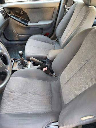 Front interior of a car showing two gray fabric seats, manual gear shift, and center console area outside the doors.