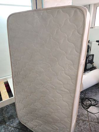 Cream-colored mattress standing upright in a room, showing a quilted wavy pattern on the surface.