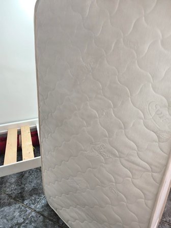 White quilted mattress standing upright beside a wooden slatted bed frame.