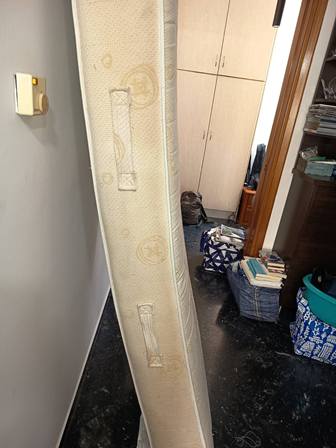Tall mattress leaning upright against a wall in a cluttered bedroom