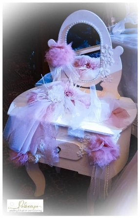 Pastel pink vanity table with a round mirror, draped in pink tulle and fluffy feathers.