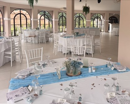 Banquet hall set for a formal event with white linens, chairs, and blue table runners under soft lighting with arched windows.