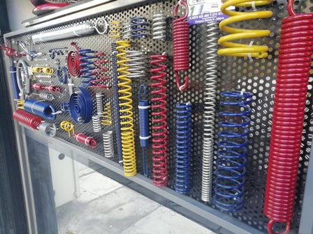 Pegboard display of assorted automotive and bike suspension springs in red, blue, yellow, and silver.