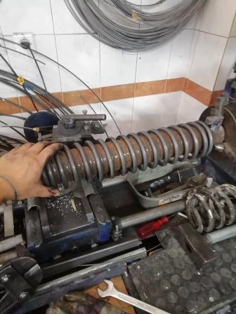 Close-up of a worker adjusting a large coil spring on a metalworking lathe in a workshop.