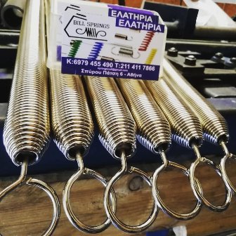 Row of shiny metal tension springs with hooks, laid on a workbench, a Greek business card resting on top.
