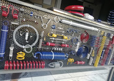 Assorted workshop tools and car parts arranged on a pegboard wall, including coil springs, hoses, wrenches, and gauges in a shop setting.
