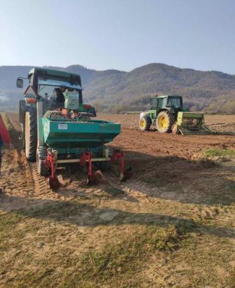 Two tractors with planting equipment on a dirt field, mountains in the background under a clear sky.