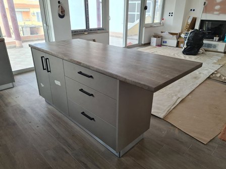 Grey kitchen island with drawers and a cabinet in a room under renovation, countertop exposed.