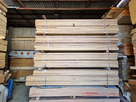 Stacks of wooden planks strapped on metal racks in a woodshop warehouse, ready for processing or sale.