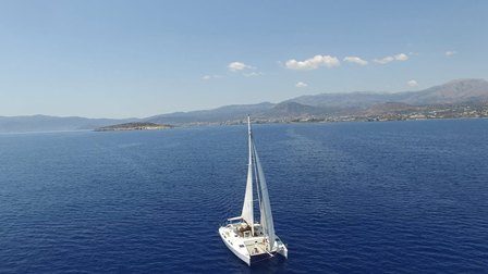 Sailboat sailing on calm blue sea with coastline and mountains in the distance.