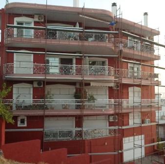 Red multi-story building under construction with scaffolding around the exterior and white balcony railings on each floor.
