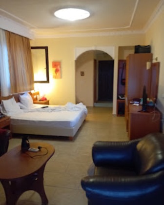 Hotel room with a double bed, nightstand, and armchair; warm yellow walls and archways in the background.