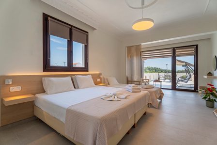 Hotel room featuring two double beds, soft lighting, and a balcony with chairs overlooking an outdoor area.