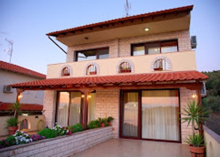Two-story villa with a red-tile roof, brick facade, large glass doors, arched windows on the upper level, and potted plants on a tiled terrace.