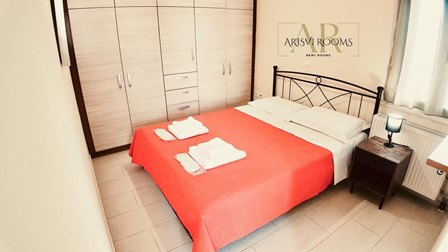 Hotel room with a double bed, orange bedspread, folded towels, and a wardrobe against the wall.