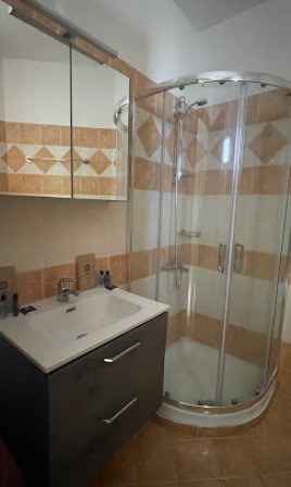Bathroom with curved glass shower enclosure beside a dark wood vanity and beige tiled walls.