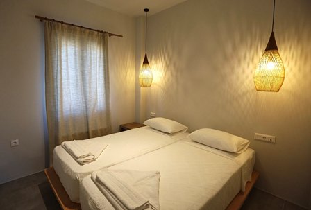 Hotel room with two single beds pushed together, white linens, beige walls, and pendant lights on each side.