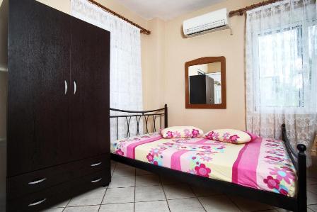 Small bedroom with a single metal-framed bed in pink floral bedding, a tall dark wardrobe, and a wall mirror above the dresser.