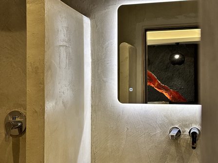 Modern bathroom with a backlit rectangular mirror, textured beige walls, and a metal sink faucet on the right.