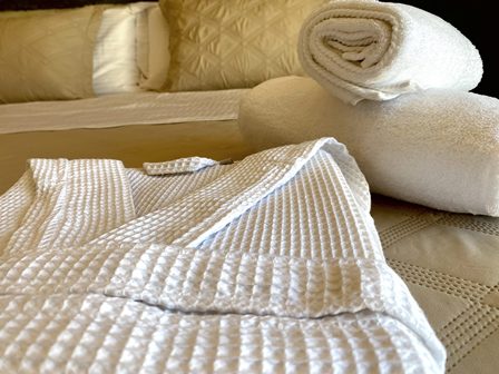 White bathrobe and rolled towels arranged on a bed in a spa-like hotel room.