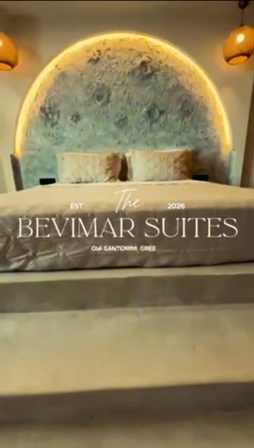 King-size bed in a modern suite with a circular, illuminated headboard and two lamps, a decorative bed runner reading 'BEVIMAR SUITES' across the foot of the bed.