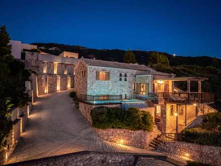 Stone hillside resort at night with warm lights along stone walls and terraces, and a lit courtyard.
