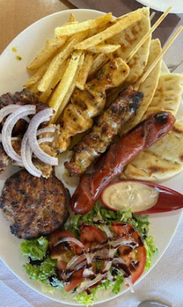 Plate of mixed grilled kebabs (chicken and beef) with grilled sausage, french fries, pita/flatbread, sliced onions, and a small greens salad with dressing on the side.