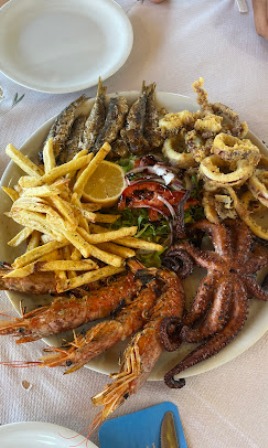 Seafood platter with fried shrimp, calamari, fries, a lemon wedge, and greens on a white plate.