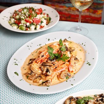 Creamy shrimp in mushroom sauce on a white plate, garnished with parsley, with a side salad and wine glass in the background.