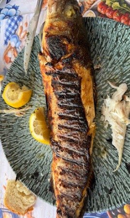 Whole grilled fish with scored, crispy skin on a blue plate, with lemon wedges nearby and a small bread piece to the side.