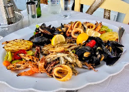 Seafood platter on a white plate with lemon wedges, including calamari rings, mussels, shrimp, and grilled fish.