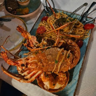 Lobster tails on a pasta dish served on a blue rectangular plate, with herbs and cherry tomatoes garnish.