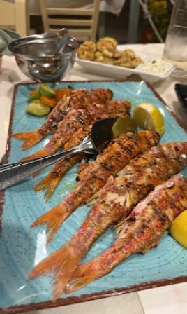 Grilled shrimp skewers on a turquoise plate with lemon wedges and dipping sauce; table setting in the background.