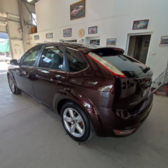 Rear three-quarter view of a dark red crossover parked inside a showroom.