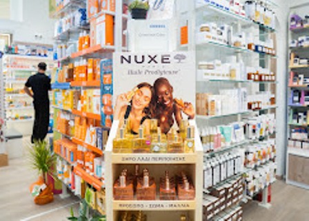 Two smiling customers pose at a NUXE beauty products display in a bright store aisle.
