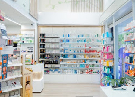Bright pharmacy interior with shelves stocked full of medicines and health products on white back wall fixtures.