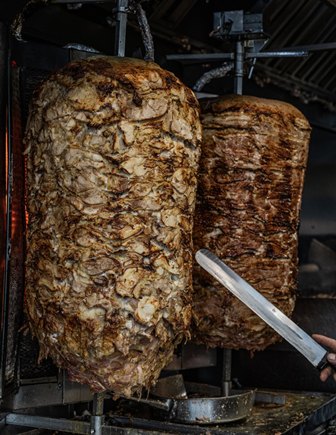 Two large beef roasts smoking in a commercial meat smoker, with a carving knife poised to slice one roast