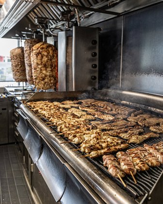 Commercial grill with rows of skewered meat cooking and rotisserie meat turning on the spit in a professional kitchen.