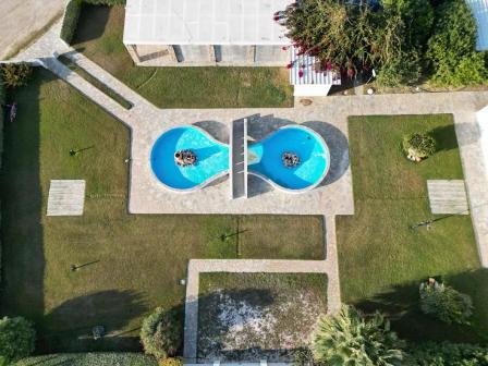 Aerial view of two circular blue pools connected by a central wall in a grassy park with walkways.