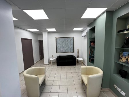 Lobby seating area with two beige armchairs facing a black sofa, tile floor, and green built-in shelves on the right.