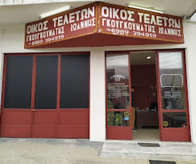 Storefront of a Greek funeral home with red doors and a red sign above the entrance.