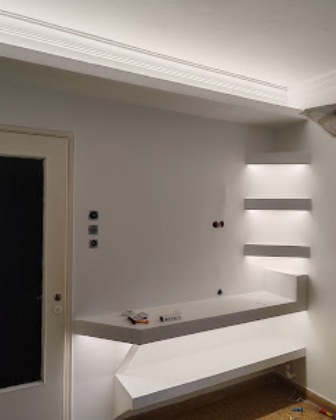 White interior corner with a floating desk and four lit wall shelves on the right; door visible on the left.