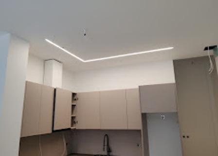 Modern kitchen under construction with beige cabinets, a black sink, and ceiling LED strip lights.