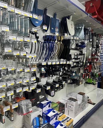 A hardware store aisle with metal and plastic kitchen tools and utensils hanging on pegboard, organized by item type and price tags visible on shelves