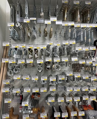 Store display wall of metal hardware with brackets, clamps, and hooks on labeled shelves and pegboard racks.