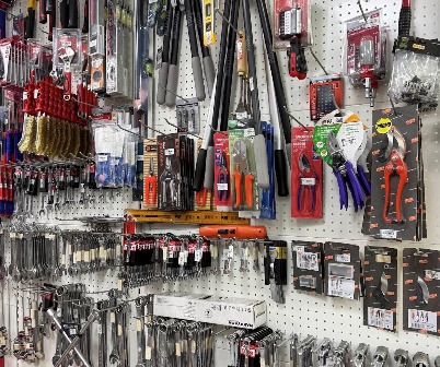 Assorted hand tools hanging on a pegboard wall in a hardware store, with pliers, blades, and packaged accessories visible.